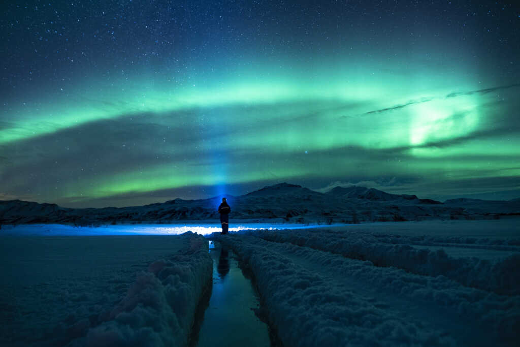 A stunning view of the Northern Lights illuminating the night sky over a snow-covered landscape in Sweden, with vibrant green and purple lights dancing above the horizon.